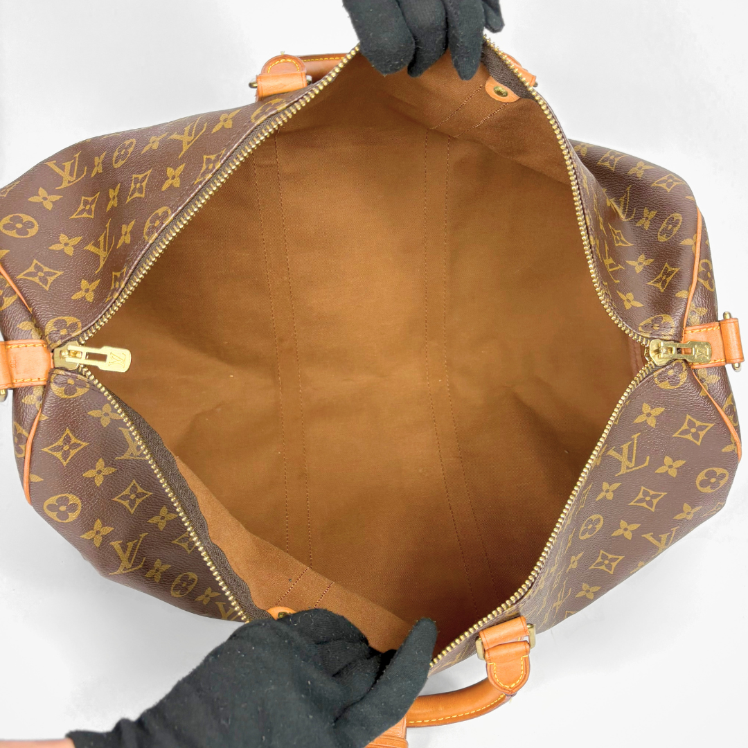 Brown leather bag with orange accents held open by gloved hands on a white background